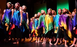 Youth choir singing on stage wearing bright rainbow colored silk ponchos.